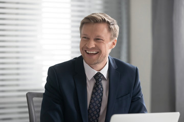 Happy cheerful businessman in suit laughing sit at work desk