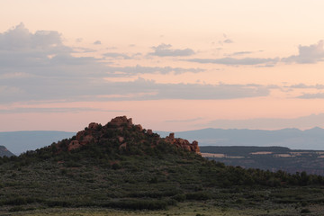A red sandstone knoll rises up above the junipers and sagebrush in the southwest desert under a sunset sky.