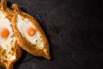 Traditional Adjarian Georgian khachapuri with cheese and egg on black background. Top view. Copyspace
