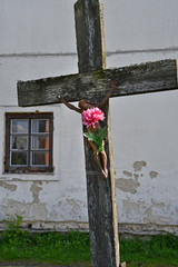 verwittertes holzkreuz mit metallkorpus und roter kunstblume