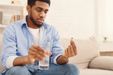 African-american man holding glass of water and looking at pill