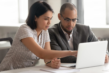 Female asian mentor teaching african male intern looking at laptop