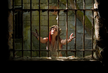 A young woman prays inside a jail ruin. She is  dressed in white and wears a thorn wreath on  her...