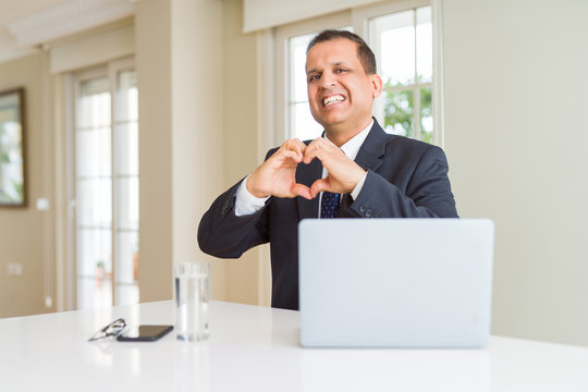 Middle age business man working with computer laptop smiling in love showing heart symbol and shape with hands. Romantic concept.