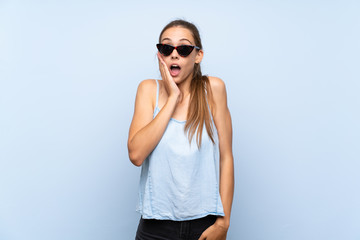 Young woman over isolated blue background with glasses and surprised