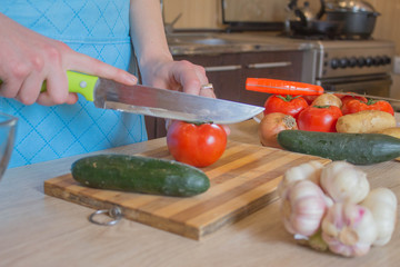 Chef cuts the vegetables into a meal. A woman uses a knife and cooks. Woman's hands cutting vegetables, behind fresh vegetables