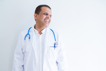 Middle age doctor man wearing stethoscope and medical coat over white background looking away to side with smile on face, natural expression. Laughing confident.