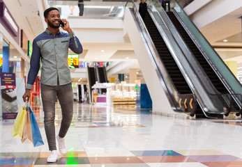 Handsome african man with shopping bags talking by cellphone