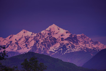 Evening view of sunset over the snowy mountain peak. Nature landscape. Dramatic overcast scene....