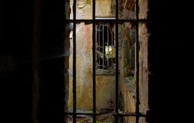 A photo of a dirty run down prison cell ruins. The bars are rusted badly and the walls are badly decayed.