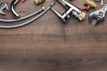 Top view of plumbing tools on brown table. Flat lay image of wrench, flexible hose connectors, mixer tap over wooden background with copy space. Upside composition of tools for plumber.