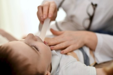 A doctor with a spatula inspects the child throat. The spatula is in the patient mouth.