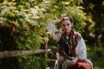 Young girl in a traditional Ukrainian dress is sitting on a bench in the park