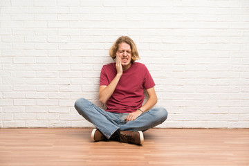 Blonde man sitting on the floor with toothache