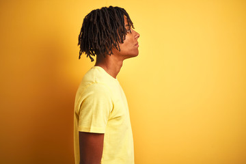 Afro man with dreadlocks wearing casual t-shirt standing over isolated yellow background looking to side, relax profile pose with natural face with confident smile.