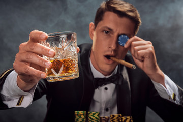 Handsome emotional man is playing poker sitting at the table in casino against a white spotlight.