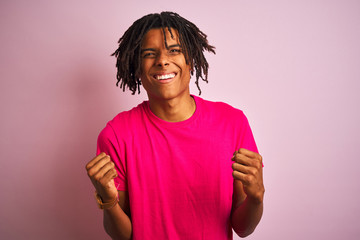 Afro american man with dreadlocks wearing t-shirt standing over isolated pink background very happy and excited doing winner gesture with arms raised, smiling and screaming for success. 