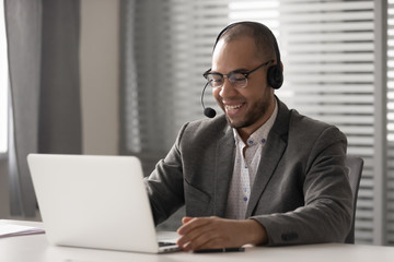 Smiling african man wearing wireless headset video calling on computer