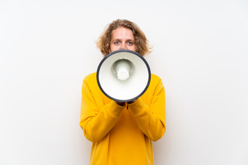 Blonde man with  sweatshirt over white wall shouting through a megaphone