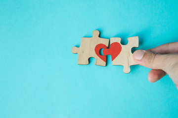 Female hand connecting puzzle with drawn red heart on blue background. Love concept. St. Valentine day. Reconciliation. Reunion concept. Copy space.