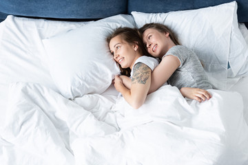 two smiling lesbians embracing while lying in bed
