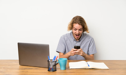 Blonde man with a laptop surprised and sending a message