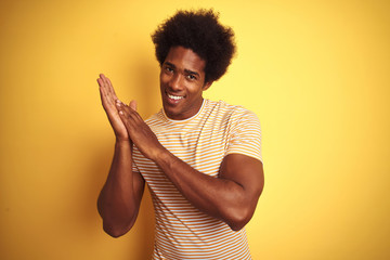 American man with afro hair wearing striped t-shirt standing over isolated yellow background...