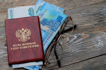 Russian money and a pension certificate and glasses . Russian translation: Pension Fund of the Russian Federation. Pensioner's ID on the wooden background, concept of pension reform, selective focus