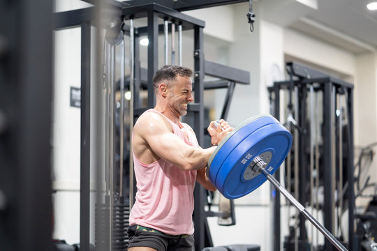 Very strong man lifting barbells in gym.