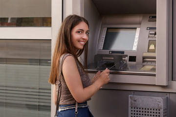 Fototapeta na wymiar Young woman in front of a bank ATM machine on the street, holding card 
