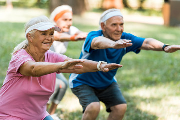 selective focus of happy multicultural senior people doing sit ups on grass