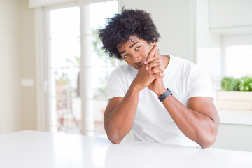 Young african american man wearing casual white t-shirt sitting at home Holding symbolic gun with hand gesture, playing killing shooting weapons, angry face