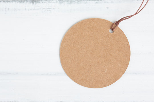 Brown round craft paper label on white wood table over white brick background with copy space.