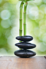 Fototapeta na wymiar Zen stones with green bamboo on wooden table with green blur bokeh background