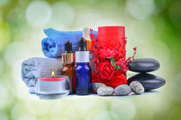 Red romantic candle and spa oil with towel and zen stone over green blur bokeh background