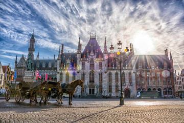 Naklejka na ściany i meble Horse carriages on Grote Markt square in medieval city Brugge at morning on background sunrise, Belgium. Shallow depth of field