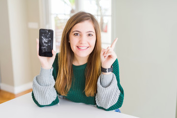 Beautiful young woman holding broken smartphone very happy pointing with hand and finger to the side