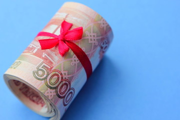 Russian money 5000 rubles twisted into a tube and tied with a ribbon, on a colored background