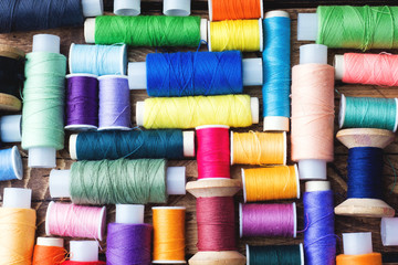 Colored spools of thread laid out in rows on wooden background.
