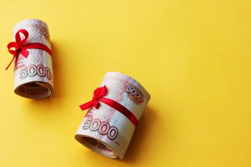 Russian money 5000 rubles twisted into a tube and tied with a ribbon, on a colored background