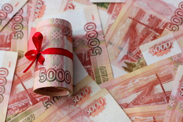 Russian money 5000 rubles twisted into a tube and tied with a ribbon, on a colored background, living coral the color of the year according to the version of Pantone