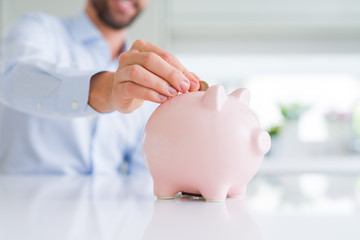 Close up of man hand putting a coin inside of piggy bank as savings