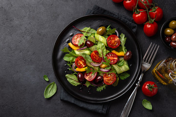 Fresh vegetable salad with tomato, cucumber, bel pepper and olives salad on black plate
