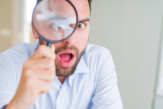 Handsome business man holding magnifying glass close to face, big eyes and funny expression