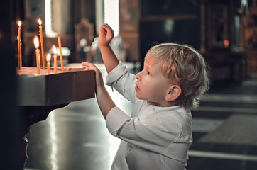 Little blonde boy in the church on Easter. Puts a candle to prays to God