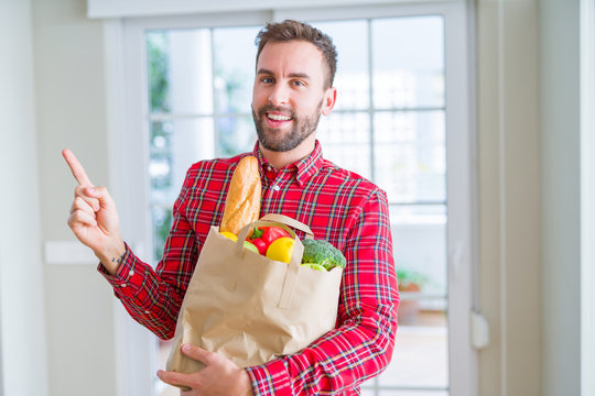 Handsome man holding groceries bag very happy pointing with hand and finger to the side