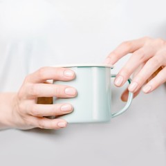 Beautiful female hands holding an enamel cup. Manicure with nude nail polish. Copy space