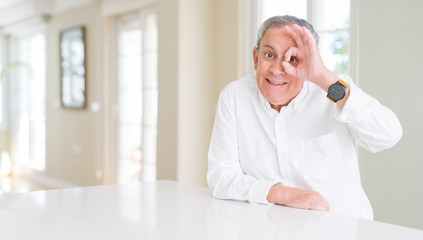 Handsome senior man at home doing ok gesture with hand smiling, eye looking through fingers with happy face.