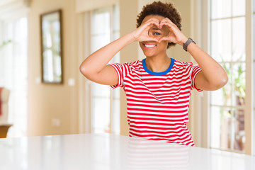 Young beautiful african american woman at home Doing heart shape with hand and fingers smiling looking through sign