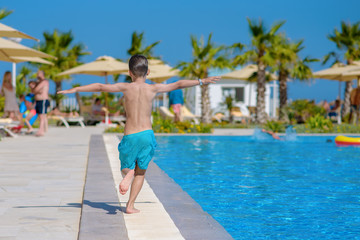 Smiling Caucasian boy having fun in swimming pool at resort on family vacation. He is running along pool edge. - 279876909